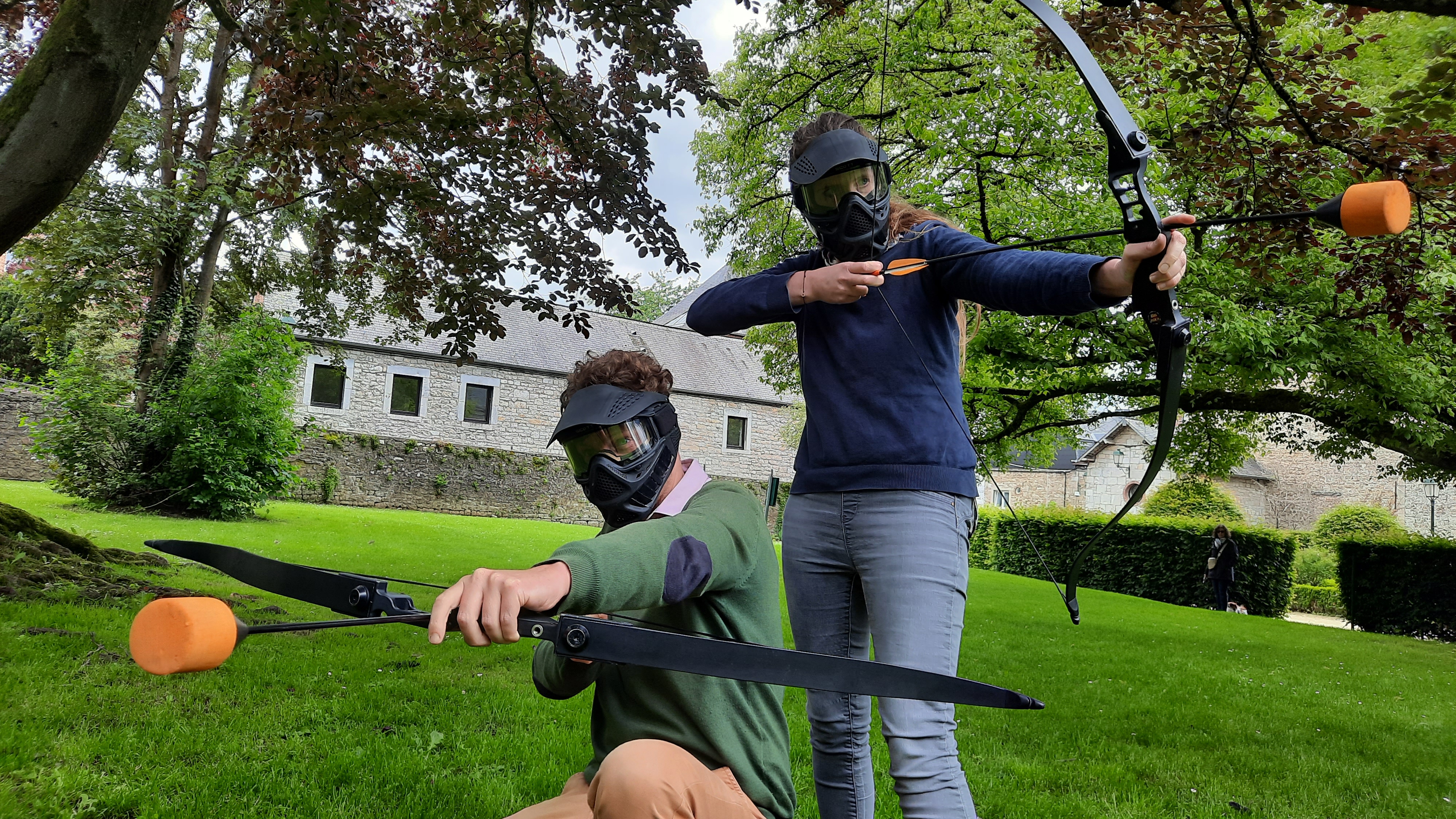 Photo de deux adultes équipés du matériel d'archery tag et prêts à tirer au Famenne & Art Museum