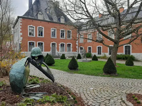 Photographie d'une sculpture en métal représentant un pingouin fantastique avec en arrière-plan la façade du Famenne &amp; Art Museum