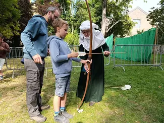 Photo d'une dame en habits médiévaux expliquant l'art du tir à l'arc à un enfant