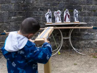 Photo d'un garçon de dos tirant sur des cibles avec une reconstitution ludique de baliste