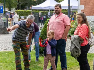 Photo d'une fillette entourée de ses parents et apprenant le tir à l'arc avec un animateur
