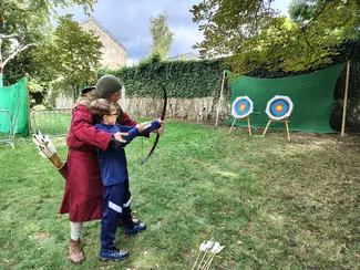 Photo d'un reconstituant habillé en archer médiéval qui initie un jeune garçon au tir à l'arc