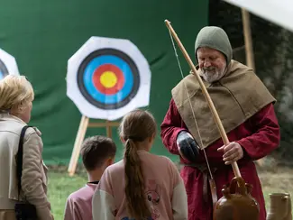 Photo d'un homme habillé en archer médiéval qui explique l'art du tir à l'arc à des enfants