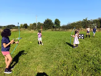 Photo de cinq enfants participant à un match d'archery tag dans une prairie