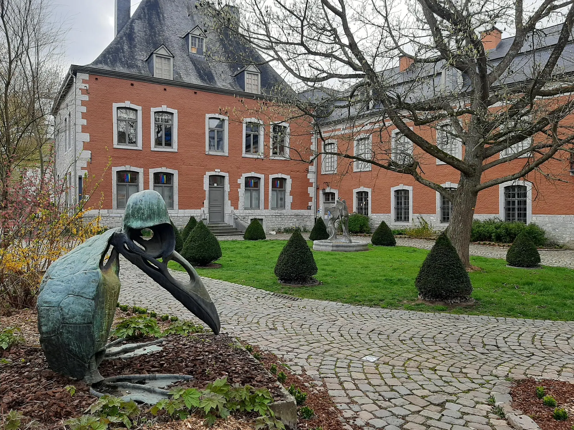 Photographie d'une sculpture en métal représentant un pingouin fantastique avec en arrière-plan la façade du Famenne &amp; Art Museum