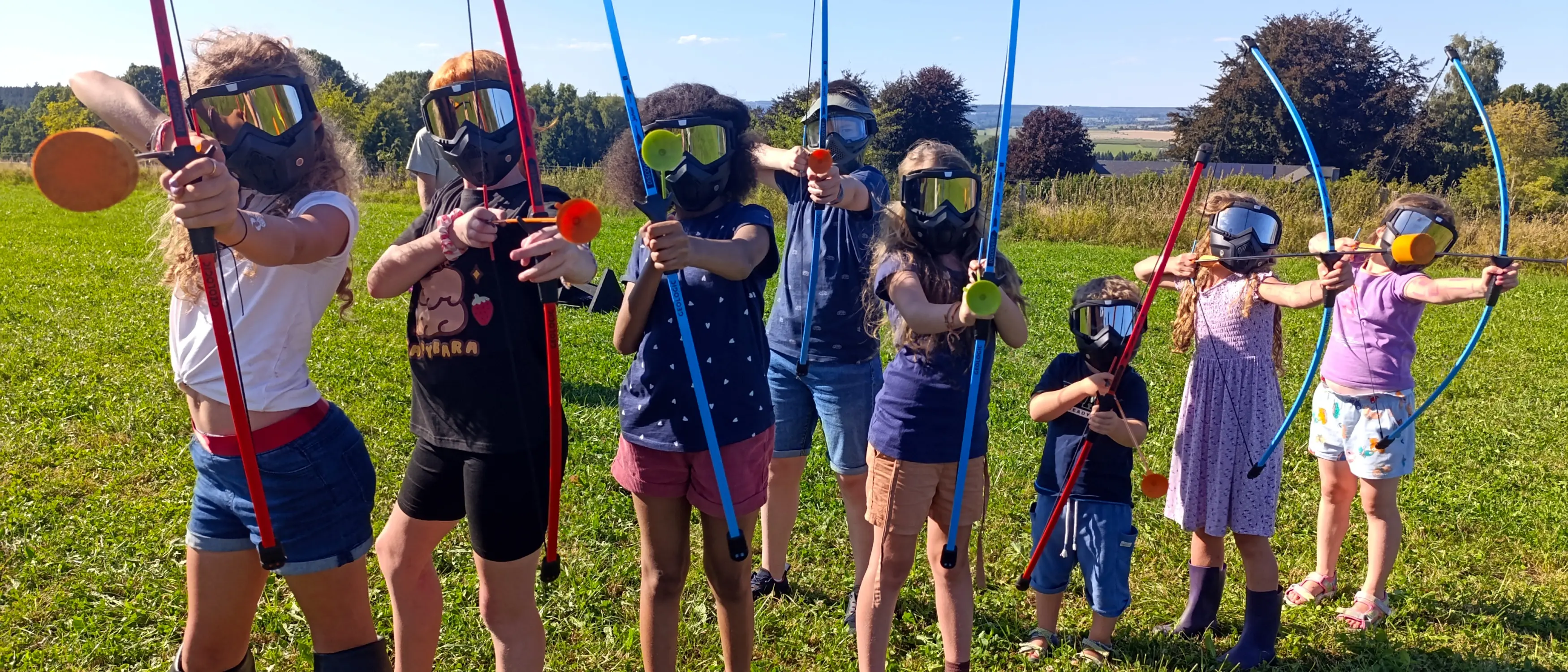 Équipés d'un masque, d'un arc et d'une flèche, huit enfants placés côte à côte sont photographiés en train de viser.